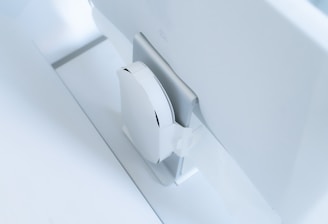 A white, sleek, vertical gaming console placed beside a large, slim monitor. The setting exudes minimalism with a focus on modern technology design.