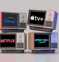 Four old-style television sets are stacked in two rows and each screen displays a different streaming service logo: Disney+, Apple TV+, Netflix, and Prime Video.