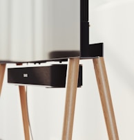 A modern television set up on sleek, angled wooden legs with a soundbar positioned directly beneath it. The design is minimalist and stylish, integrating functionality with aesthetics in a clean, contemporary space.